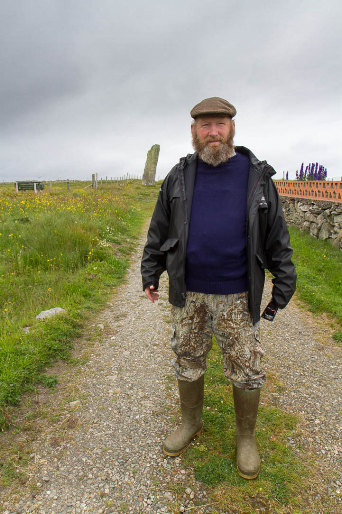 un Ecossais pose devant chez lui avec un menhir